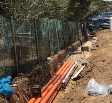 construction along a depot fence line with plastic piping lying in a trench